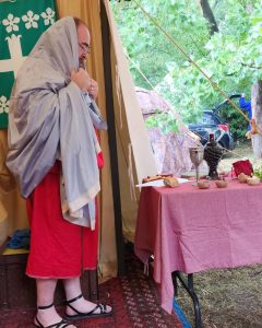Baron Angus not wearing his black linen tunic at Julia Fortunata's naming ceremony during Canterbury Faire AS 57.
Angus is wearing a red linen tunic, with a mauve silk head covering and black sandals.