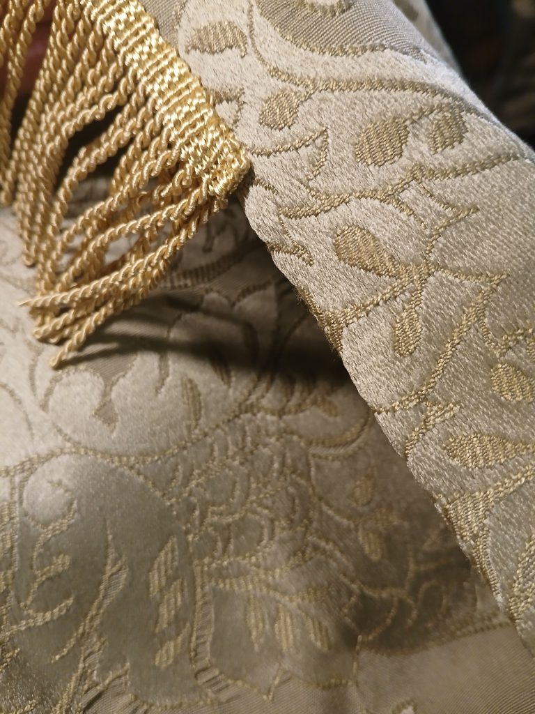 Green brocade fabric with a portion of gold bullion fringe attached at the hem