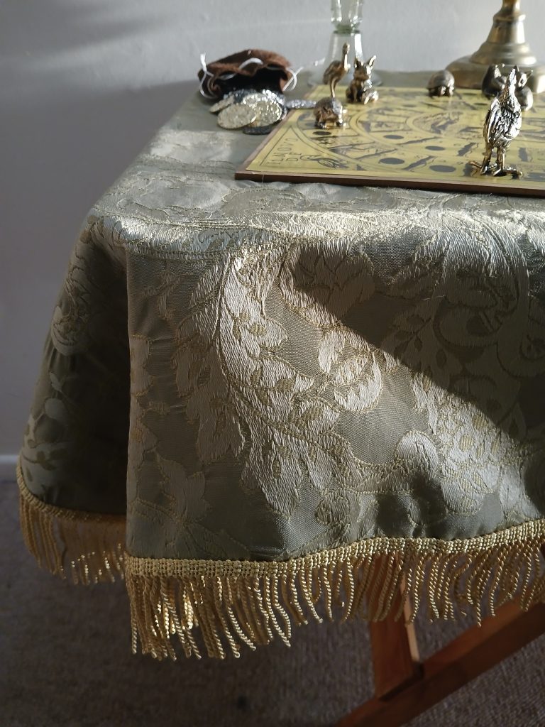 Isabel Maria's entry in the UFO Challenge, in the category "I just couldn't wait" is A green brocade tablecloth with a gold fringe at the hem on a small, wooden folding table with game pieces and a drinking glass on top