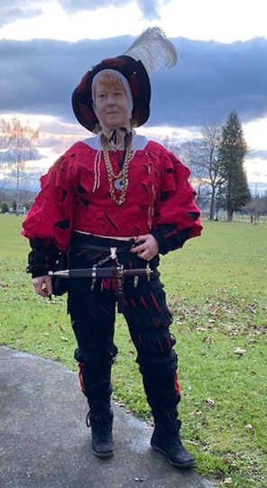 Meistern Christian Baier wearing a male landsknect ensemble comprising a red wams, black hosen and underhosen, black hat with feathers over a linen coif